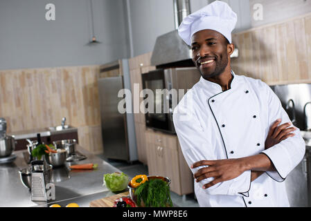 African american chef standing with arms folded by table with cooking ingredients Stock Photo