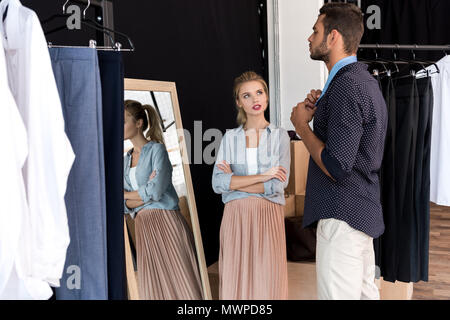 young woman looking at boyfriend trying on necktie in boutique Stock Photo