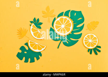 Tropical leaves pattern. Green monstera and fern leaves with orange and lemon slices on a bright yellow background. Summer vacation concept with paper craft fruits Stock Photo