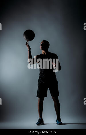 african american sportsman spinning basketball ball on finger in dark room Stock Photo