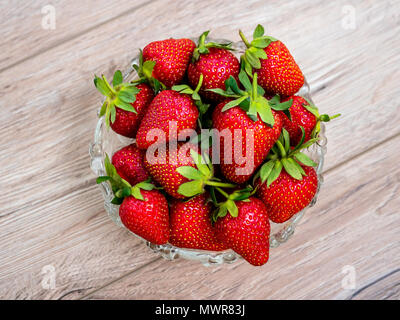 Heap of fresh strawberries in glass bowl on rustic white wooden background. Stock Photo