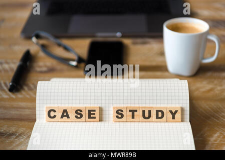 Closeup on notebook over wood table background, focus on wooden blocks with letters making Case Study text. Stock Photo