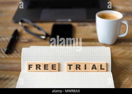 Closeup on notebook over wood table background, focus on wooden blocks with letters making Free Trial text. Stock Photo