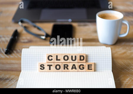 Closeup on notebook over wood table background, focus on wooden blocks with letters making Cloud Storage text. Stock Photo