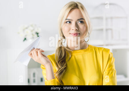 dreamy businesswoman in yellow blouse holding paper plane Stock Photo