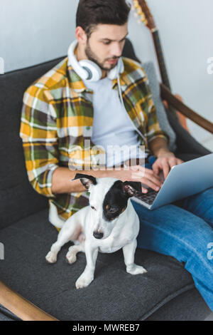 man using laptop while sitting on sofa with jack russell terrier Stock Photo