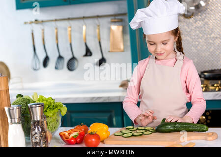 smiling kid in chef hat and apron cooking vegetable salad in kitchen Stock Photo