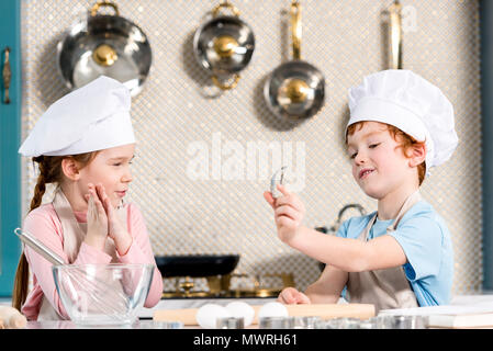 adorable children in chef hats and aprons cooking together in kitchen Stock Photo