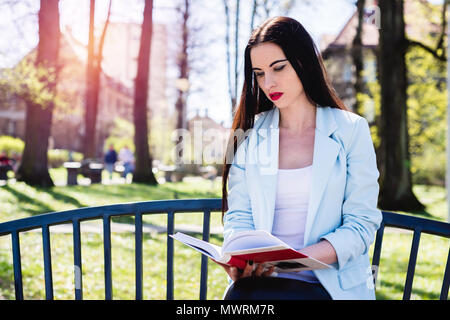 A woman is reading a book. A young and attractive girl learns to take exams at the university. Female relaxes reading interesting knowledge. The conce Stock Photo