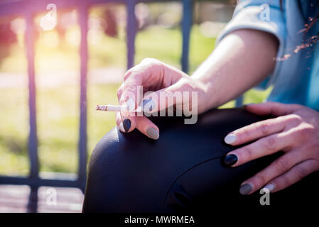 Closeup of a woman's face smoking a cigarette. An attractive girl in sunglasses holds a cigarette in her mouth. Stressed female satisfies nicotine cra Stock Photo
