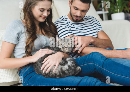 beautiful young couple petting cat at home while sitting on floor Stock Photo