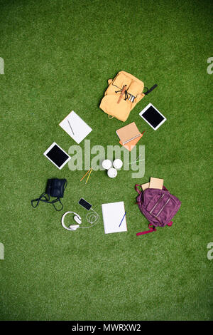 top view of arranged digital devices, backpacks and notebooks on green lawn Stock Photo