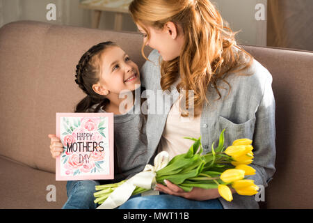 happy mother and daughter holding yellow tulips and happy mothers day greeting card Stock Photo