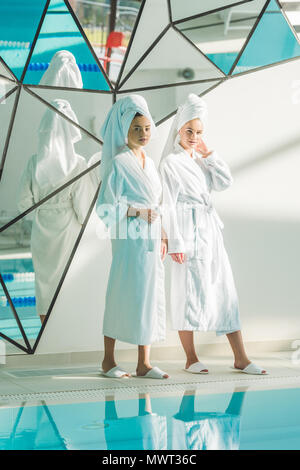 beautiful young women in bathrobes standing next to swimming pool at spa center Stock Photo