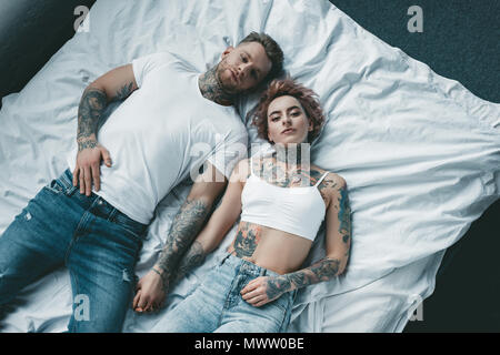 top view of young tattooed couple holding hands and lying on bed Stock Photo