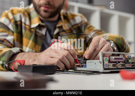 cropped image of man using multimeter while fixing broken computer Stock Photo