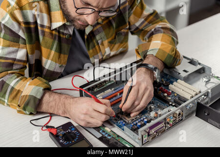 cropped image repairman using multimeter while fixing computer motherboard Stock Photo