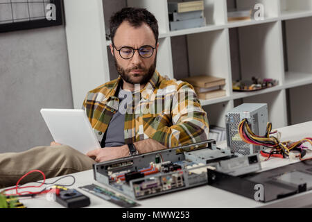 man using digital tablet while sitting against broken pc on table Stock Photo