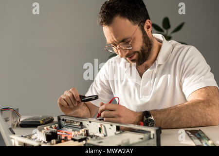 repairman using magnifier and multimeter while fixing pc Stock Photo