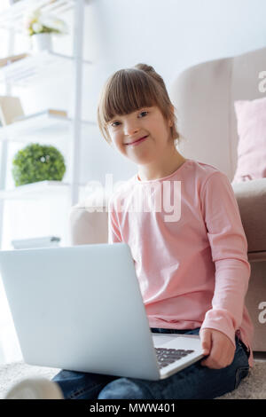 Smiling kid with down syndrome using laptop Stock Photo
