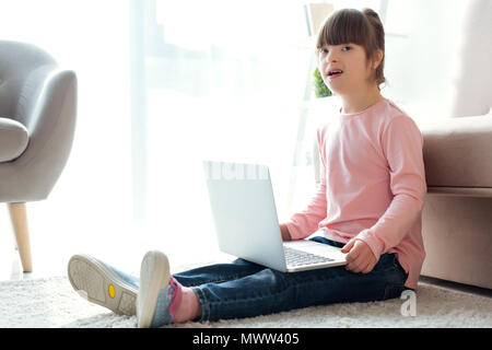 Child with down syndrome using laptop while sitting on the floor Stock Photo