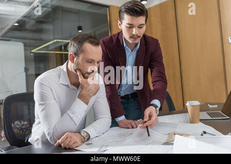 thoughtful architects brainstorming over building plans at office