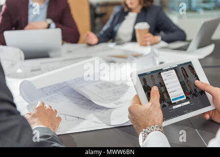 cropped shot of architect using tablet with linkedin website on screen while having conference Stock Photo