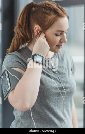 Curvy girl with fitness tracker listening to music in gym