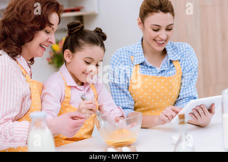 three generations of happy women in aprons preparing dough together at kitchen Stock Photo