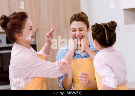 three generations of laughing women playing with flour at kitchen Stock Photo