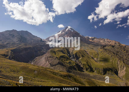 Kazbek mountain in Georgia at sunset with clouds on sky and grass on hills Stock Photo