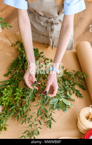 cropped shot of young florist in apron arranging green plants in flower shop Stock Photo