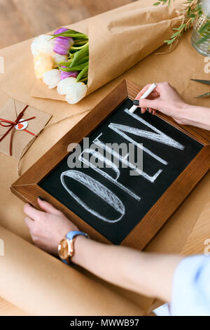 cropped shot of young florist writing word open with chalk on board Stock Photo