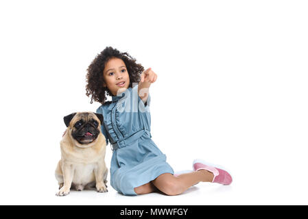 little child in dress sitting on floor with pug and pointing somewhere isolated on white Stock Photo