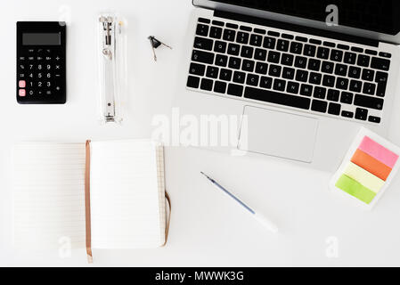 directly above shot of white desk with notebook, calculator, note pad and office supplies Stock Photo