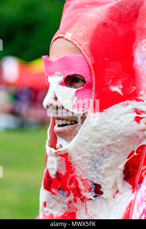 Close up of man's face after being hit on the side by a custard pie during the world custard pie championships. Young man is wearing pink mask over his eyes, and red hat surround entire face, custard seamed over mask and face. Stock Photo