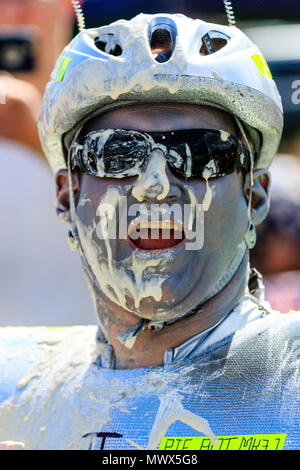 World Custard Pie Championship. Man, member of 'The Piebots' team, looking at viewer after taking a direct hit in the face with a custard pie. Wears sunglasses, and shouting, custard covering nose and splattered on cheeks and chin. Stock Photo