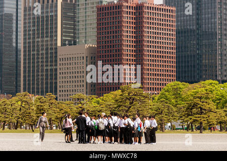 Japanese school group visiting the Imperial Palace in Tokyo with the skyscrapers of Chiyoda, Japan in the background Stock Photo