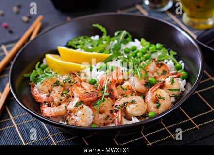 Rice with young green peas, shrimps and arugula in black bowl. Healthy food. Buddha bowl Stock Photo