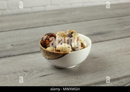 Spotted quail eggs in small porcelain bowl on gray wood desk. Stock Photo
