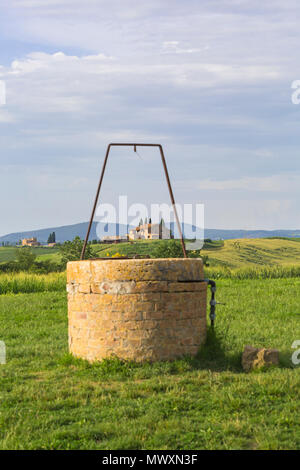 Well by old church of Vitaleta framing farmhouse buildings at San Quirico d'Orcia, near Pienza, Tuscany, Italy in May Stock Photo