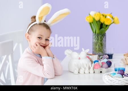 Kid in bunny ears by table with Easter eggs Stock Photo