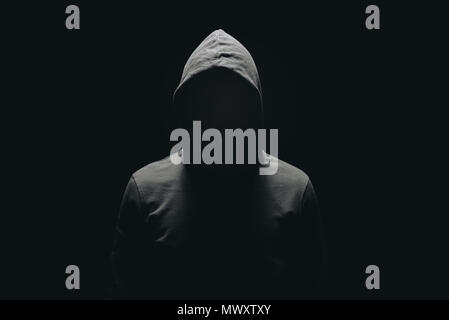 faceless man in hoodie standing isolated on black Stock Photo