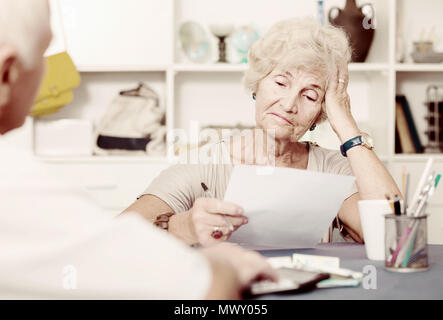 Upset senior woman sitting at home table discussing with husband their bills Stock Photo