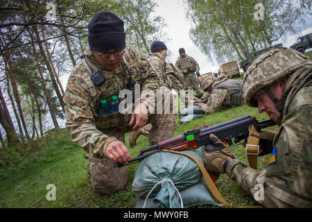 Sgt. David McLaughlin, a Soldier with the 45th Infantry Brigade Combat Team and a resident of Yukon, Oklahoma, places a coin on the barrel of a Ukrainian soldier's weapon during marksmanship instruction at the Yavoriv Combat Training Center on the International Peacekeeping and Security Center, near Yavoriv, Ukraine, on April 29.   McLaughlin's company is paired with a Ukrainian company of the 1st Airmobile Battalion, 79th Air Assault Brigade and on April 29, U.S. Soldiers mentored the Ukrainian troops on soldier skills while Ukrainian CTC staff taught the company how to employ grenades on the Stock Photo