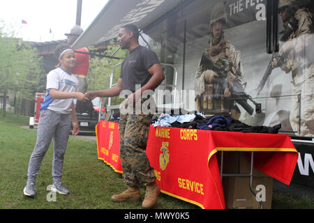 SSgt. Lonny Washington-Paige, a recruiter with Recruiting Sub-Station Tun Tavern, hands a Marine shirt to Ciara Thomas, an athlete, April 29, 2017, in Philadelphia, Pennsylvania, during the 2017 Penn Relays. The Marines handed out hundreds of shirts, protein shakers, water bottles, hats, keychains, pencils, and racing jackets to athletes throughout the three day event. In order to receive an item, athletes had to perform pull-ups or a flexed-arm hang on the pull-up bar. Stock Photo