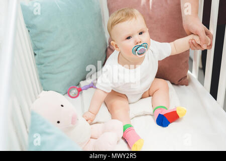 Cropped image of mother holding infant daughter sitting in crib Stock Photo