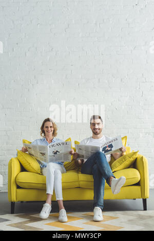 Young businessman with girlfriend sitting on sofa and reading newspaper about travel and business Stock Photo