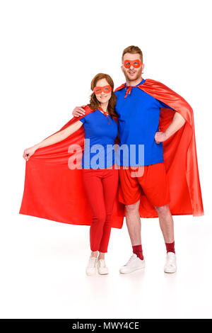 super couple in masks and cloaks standing together and smiling at camera isolated on white Stock Photo