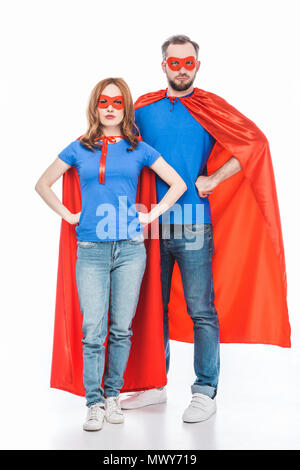 super couple in masks and cloaks standing with hands on waist and looking at camera isolated on white Stock Photo